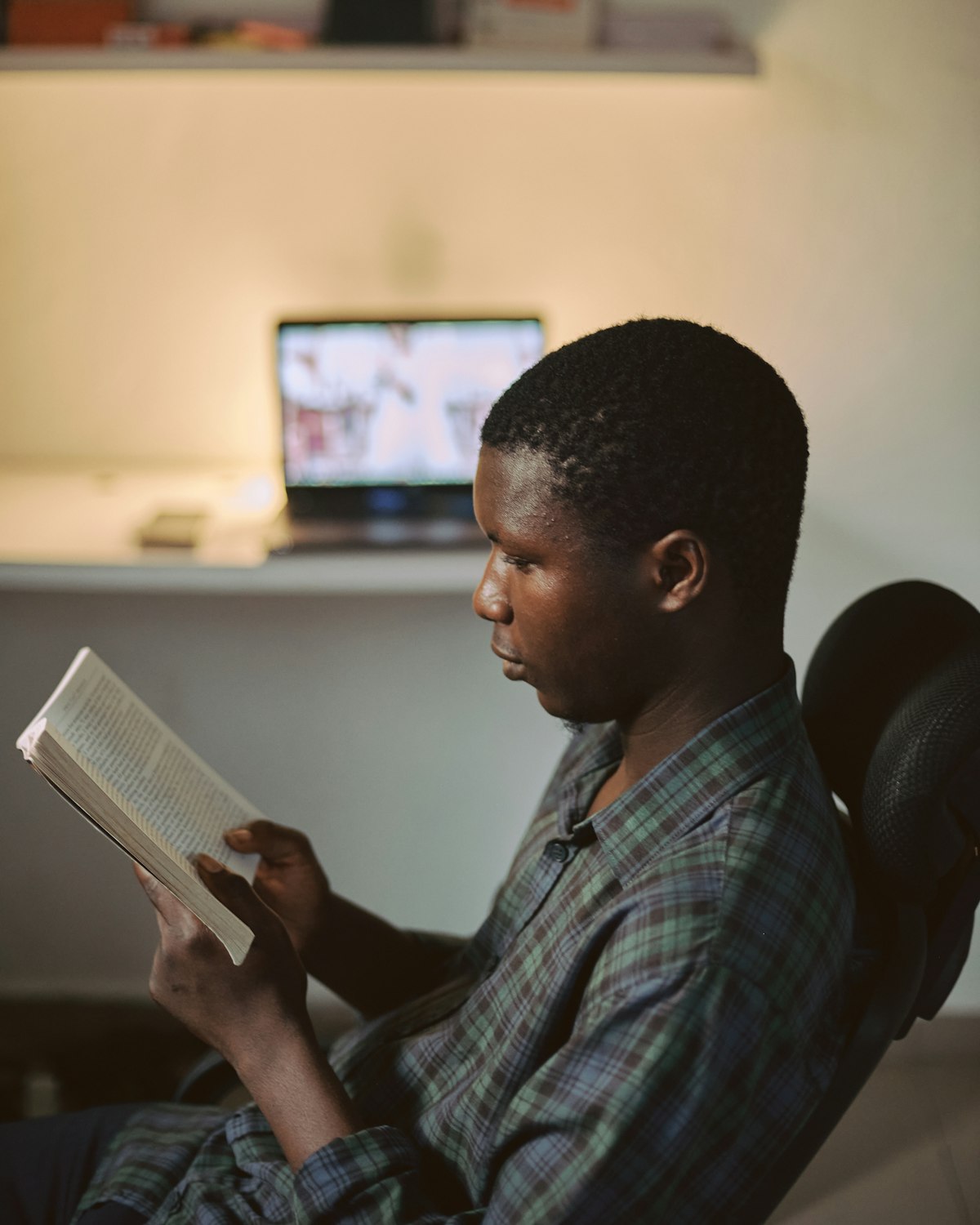 A student reading a book beside an open laptop